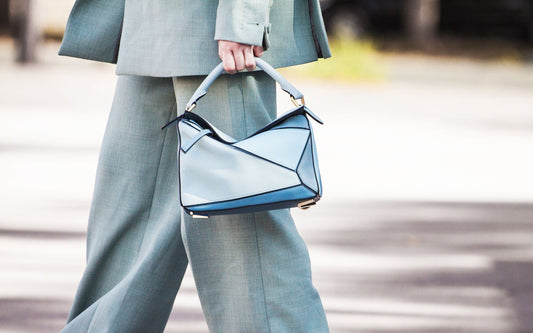 Femme portant un sac à main bleu au design géométrique, tenue en costume gris clair.